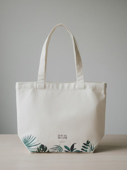 Back of the white cotton canvas tote bag featuring a vibrant, artistic print of green tropical leaves across the bottom and side