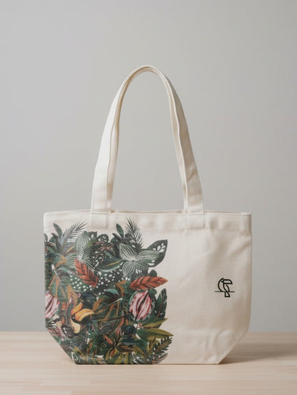 A white cotton canvas tote bag featuring a vibrant, artistic print of green tropical leaves across the bottom and side